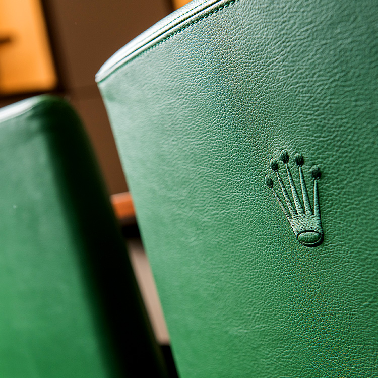 Rückseite der Rückenlehne eines grünen Lederstuhls, die mit einer Rolex Krone bestickt ist.
