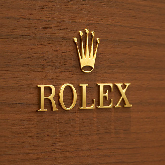 Rolex Krone mit Rolex Schriftzug darunter. Beides in Gold auf Holz angebracht.